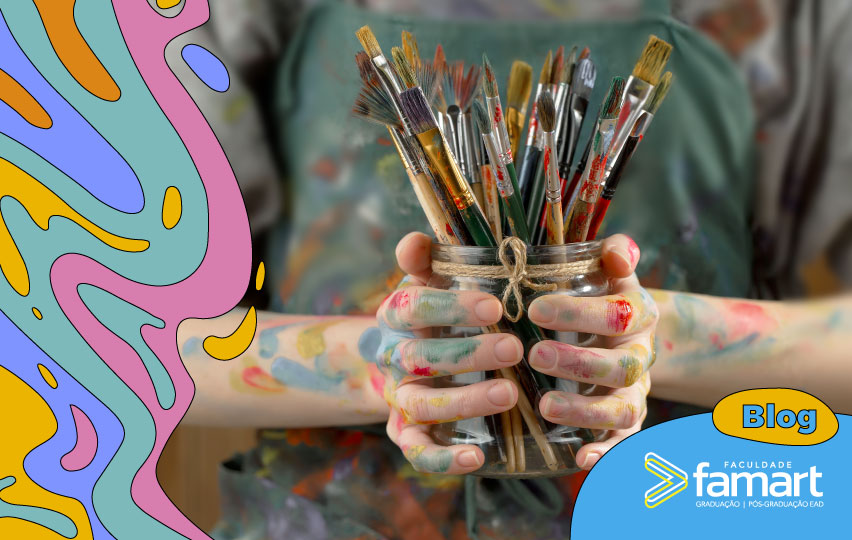 imagem de uma pessoa segurando um pote com vários pincéis e as mão sujas de tinta colorida.